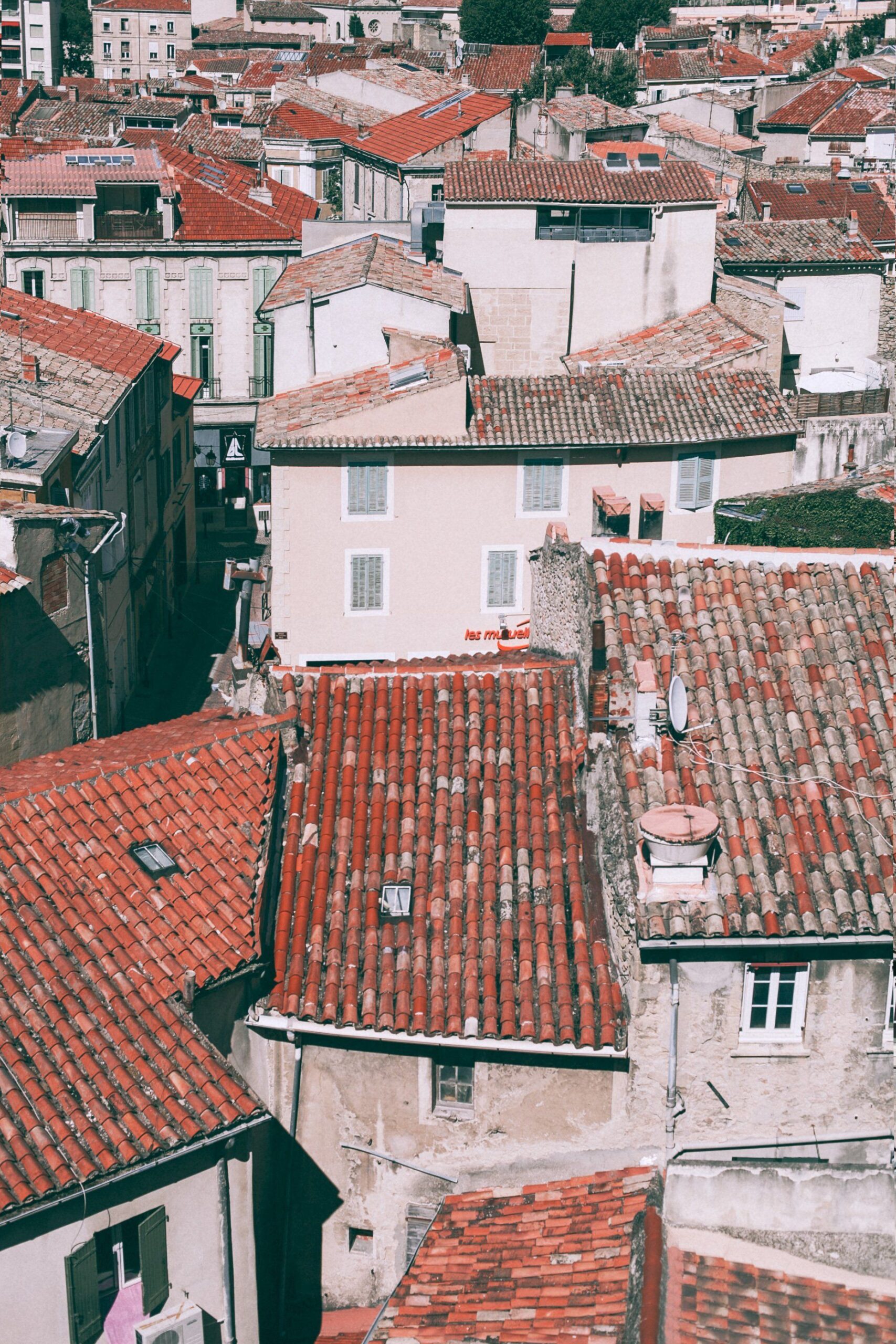 Vista elevada de edificios con tejados de tejas rojizas, fachadas claras, ventanas, chimeneas y antenas parabólicas.